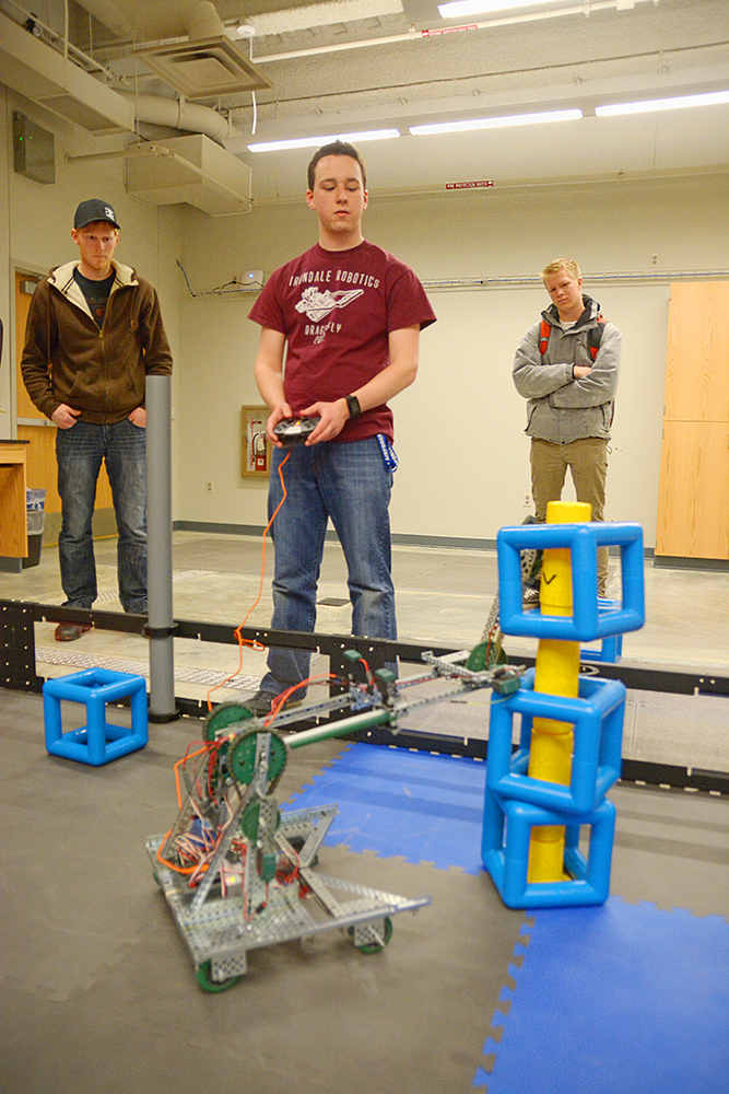 Logan Mildenberger of Husky Team 2 maneuvers a robot to put a block onto a tower of pegs as teammates Todd Hillukka and Paul Wuollet watch. 