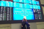 Two students stand in front of a large screen at the Tokyo Stock Exchange welcoming St. Cloud State business students
