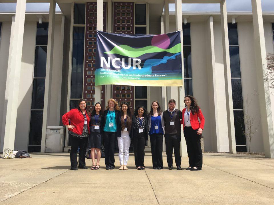 The student researchers stand in front of an NCUR sign outside the conference