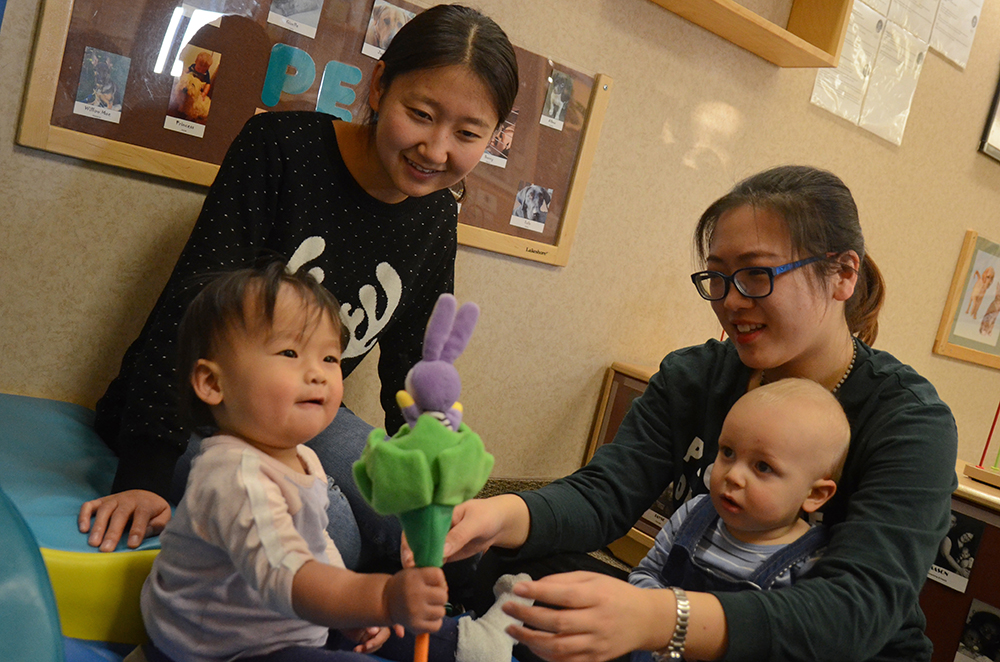 Baby Kylie Yang looks at a flower toy while volunteers Naishui Zhang and Siyu Zhao and another baby look on