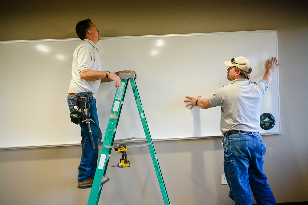 Construction workers installing a white board on a wall