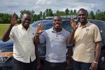 Three men standing before a car and waving