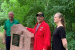 Three people stand next to a granite monument