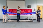 A man cuts a large blue ribbon in front of a Nahan University sign