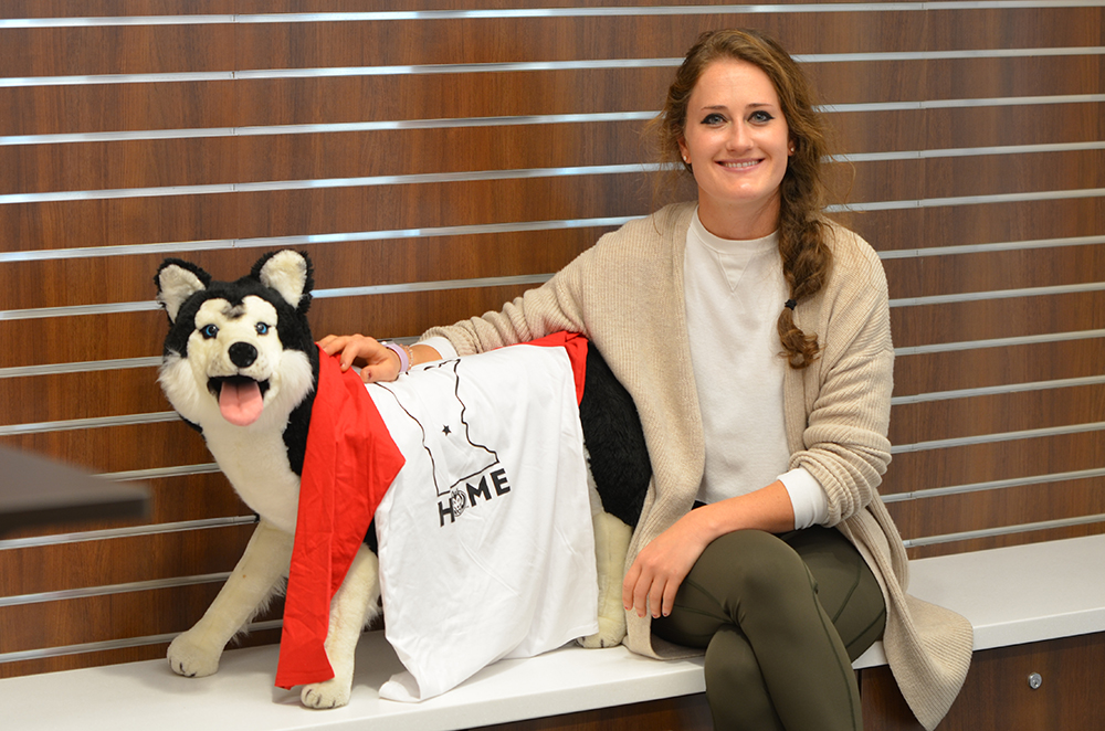 Krista Tomford sits with a stuffed animal husky and a St. Cloud State Home T-shirt in the Healthy Huskies space