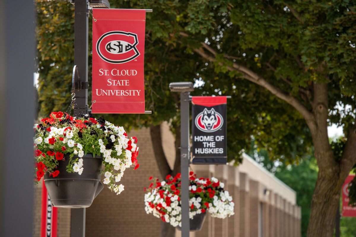 A St. Cloud State University red banner and Home of the Huskies black banner hang above red and white pots of flowers.