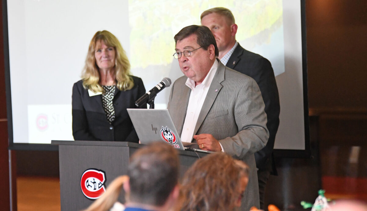 Interim President Larry Dietz, wearing a grey blazer and white dress shirt and glasses, speaks in front of a microphone