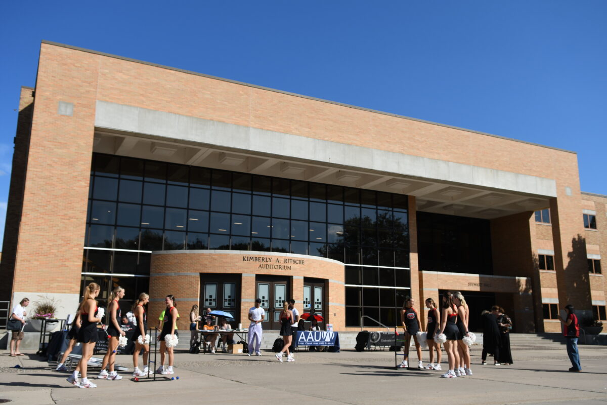 A group of students stand on the Atwood Mall with Stewart Hall and a blue sky in the background