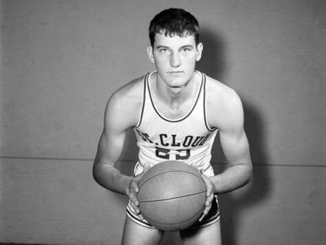 Issy Schmiesing in a white St. Cloud jersey holds a basketball and stares at the camera