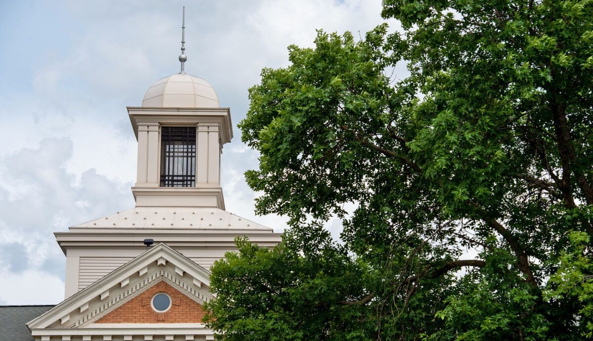The white cupola of Lawrence Hall stands against a cloudy sky and green tree branches.