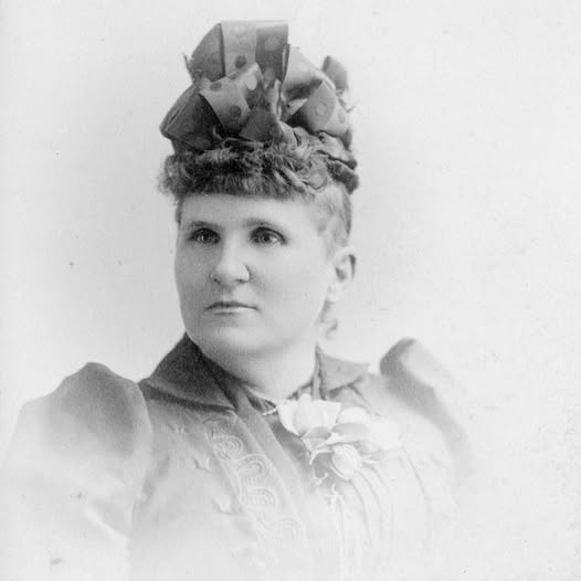 A black and white photo of a woman staring to the side with large ribbons in her hair