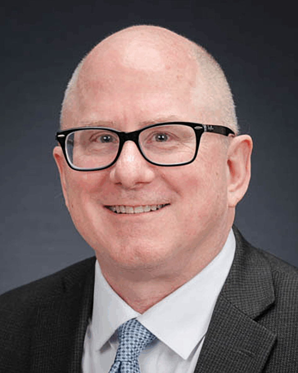 A man with glasses and wearing a suit smiles for a headshot