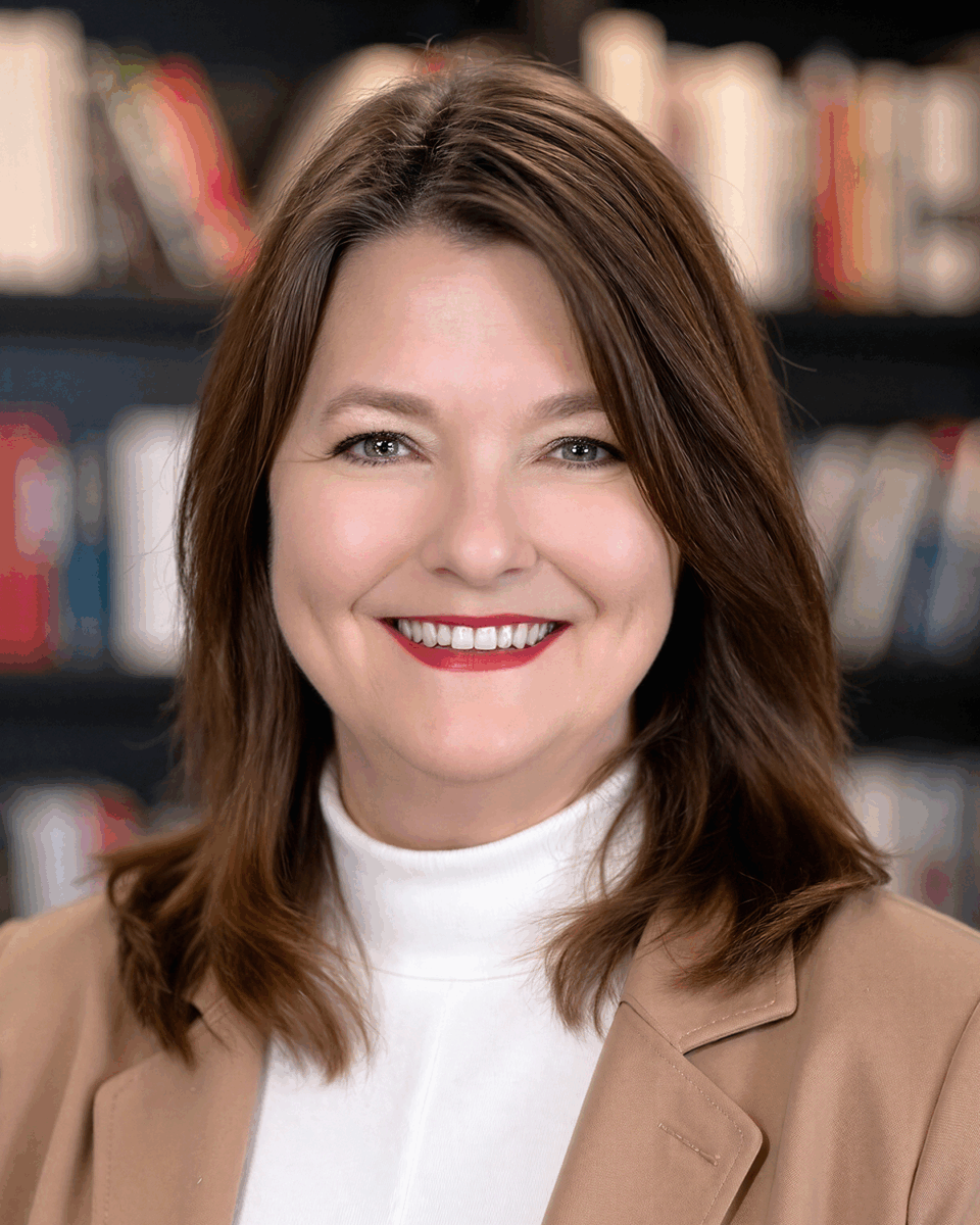 A woman with brown hair and a tan blazer smiles for a headshot
