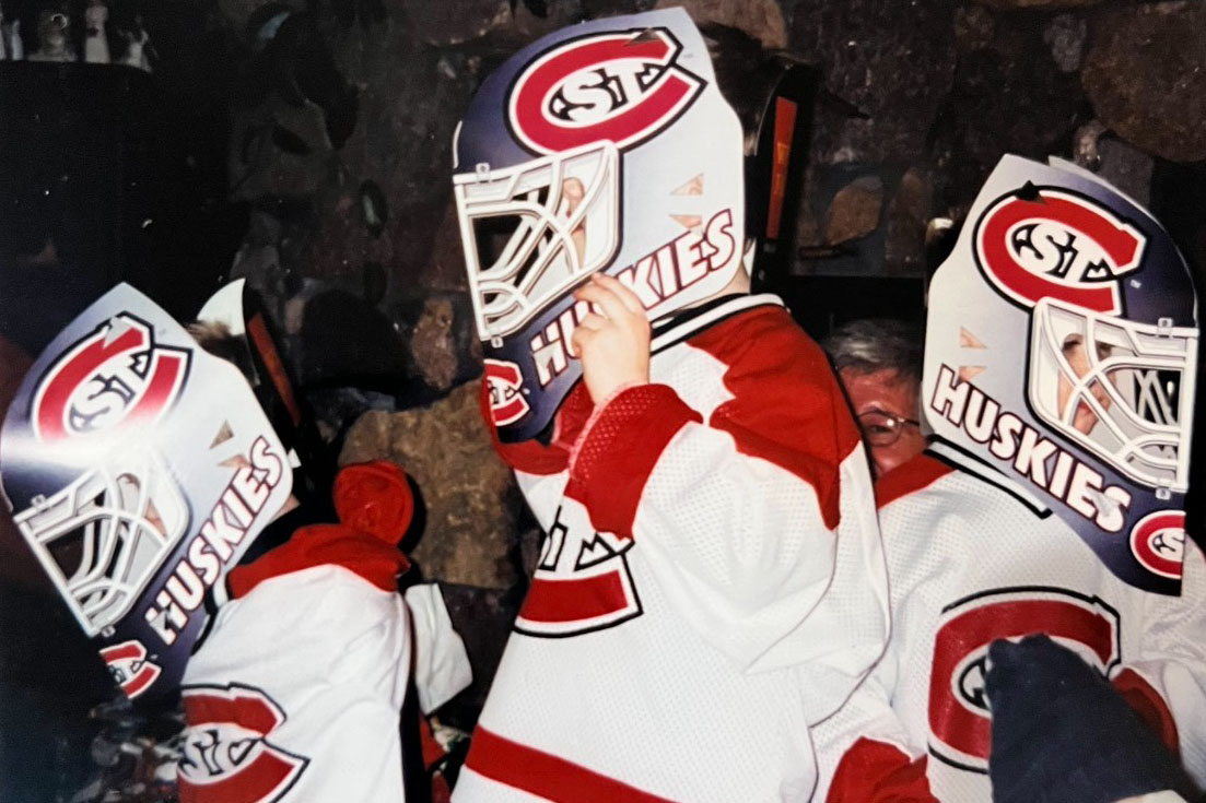Three children wear red and white SCSU jerseys with Huskies goalie helmets over their heads