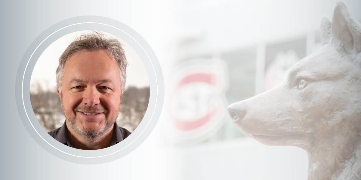 A man with a beard smiles in a circular frame next to the husky head in husky plaza