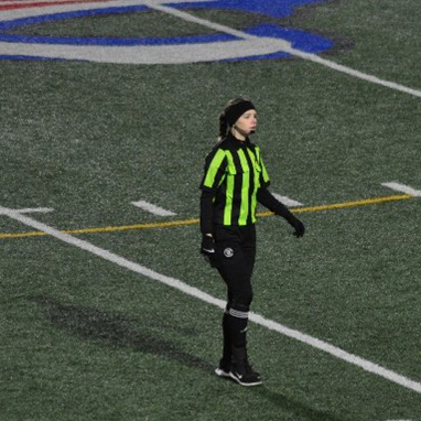 Mia Clark, wearing a yellow and black striped ref top, watches a play.