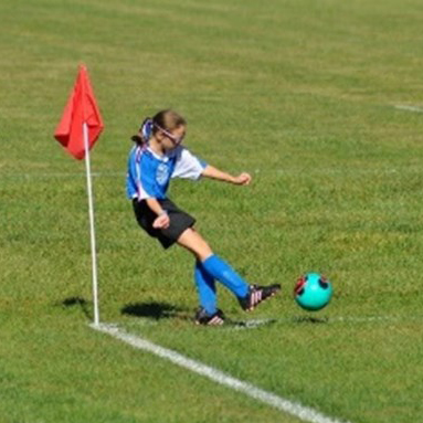 Mia Clark, wearing a blue jersey, kicks the ball as a youth soccer player