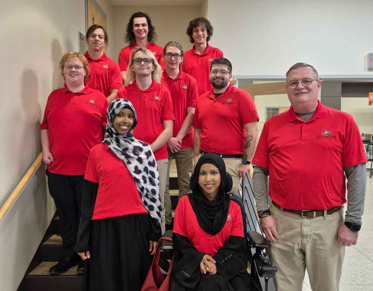 A group of 10 people wearing red shirts smile for a photo on a staircase