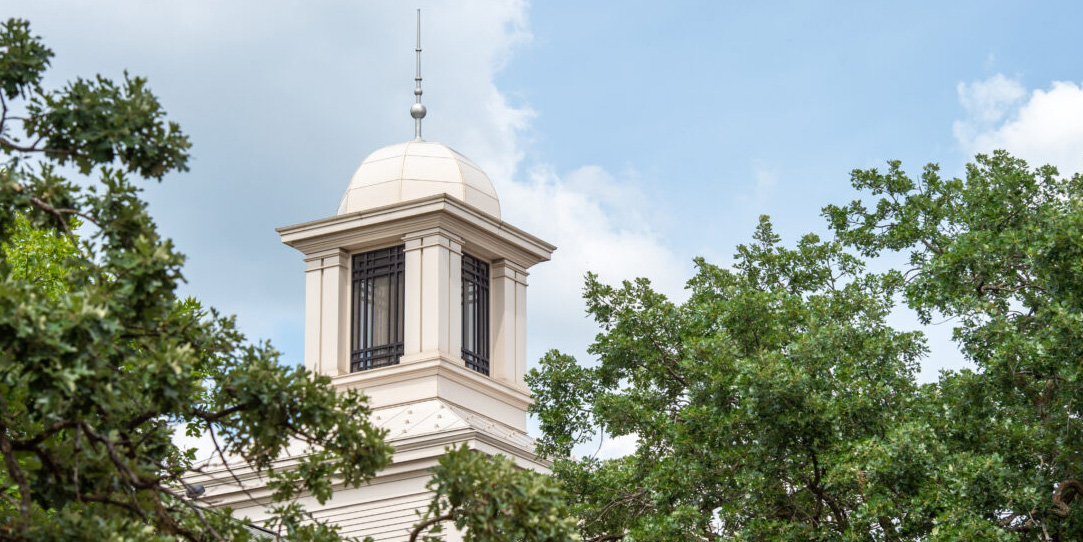 The cupola of Lawrence Hall is visible through trees on a sunny, cloudy day