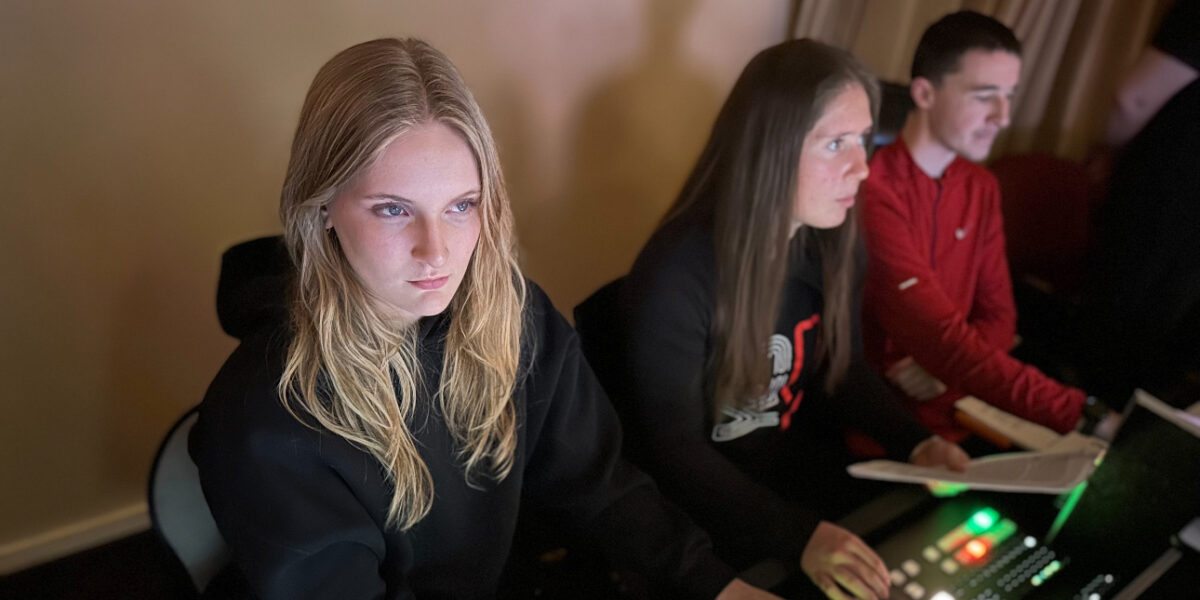 Mya Fryckman, wearing a black hoodie, works at a sound board next to two other students