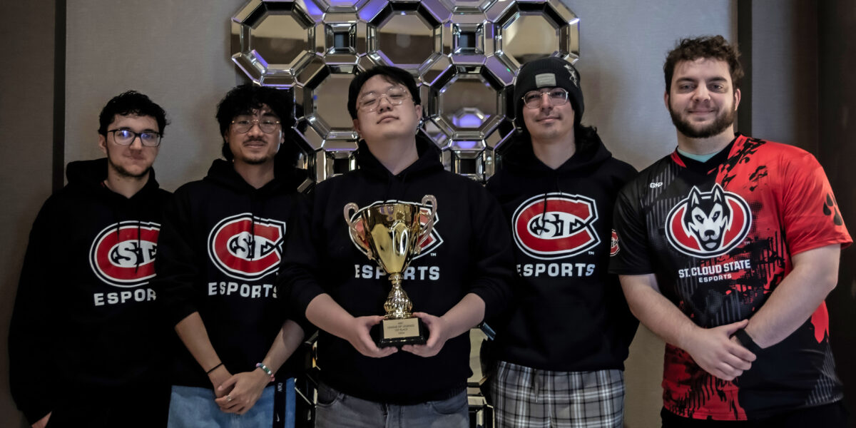 Five men wearing SCSU Esports gear smile for a photo while the man in the center holds a trophy