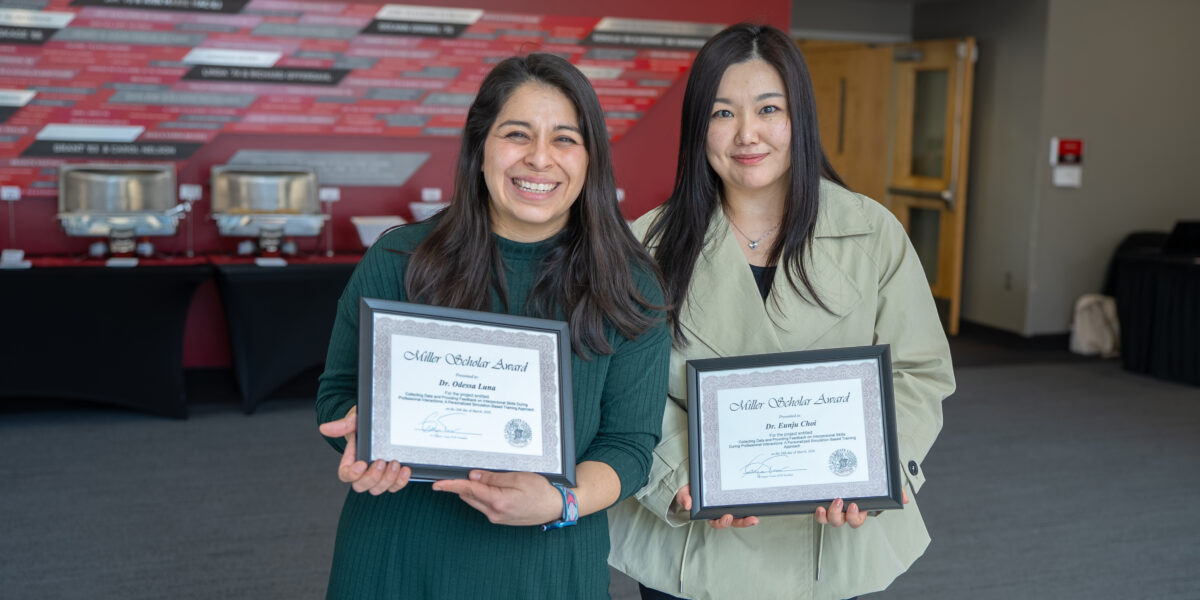 Two women smile for a photo while holding framed Miller Scholar Award certificates