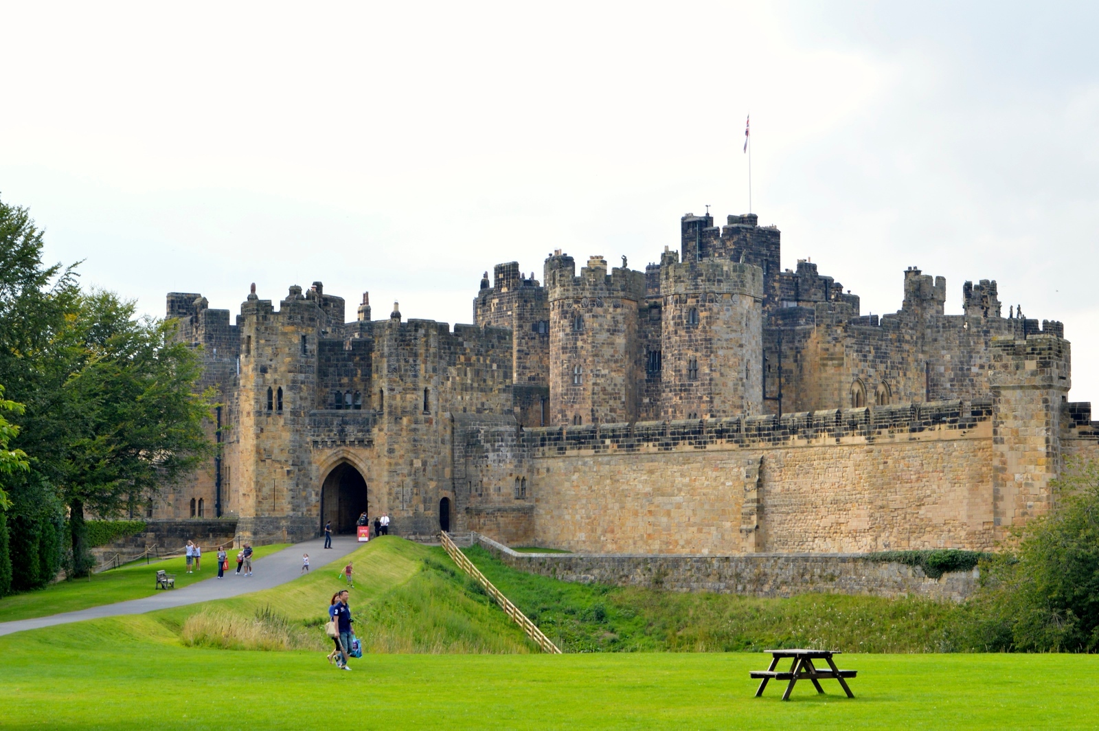People wandering lush green lawns in front of a large castle.