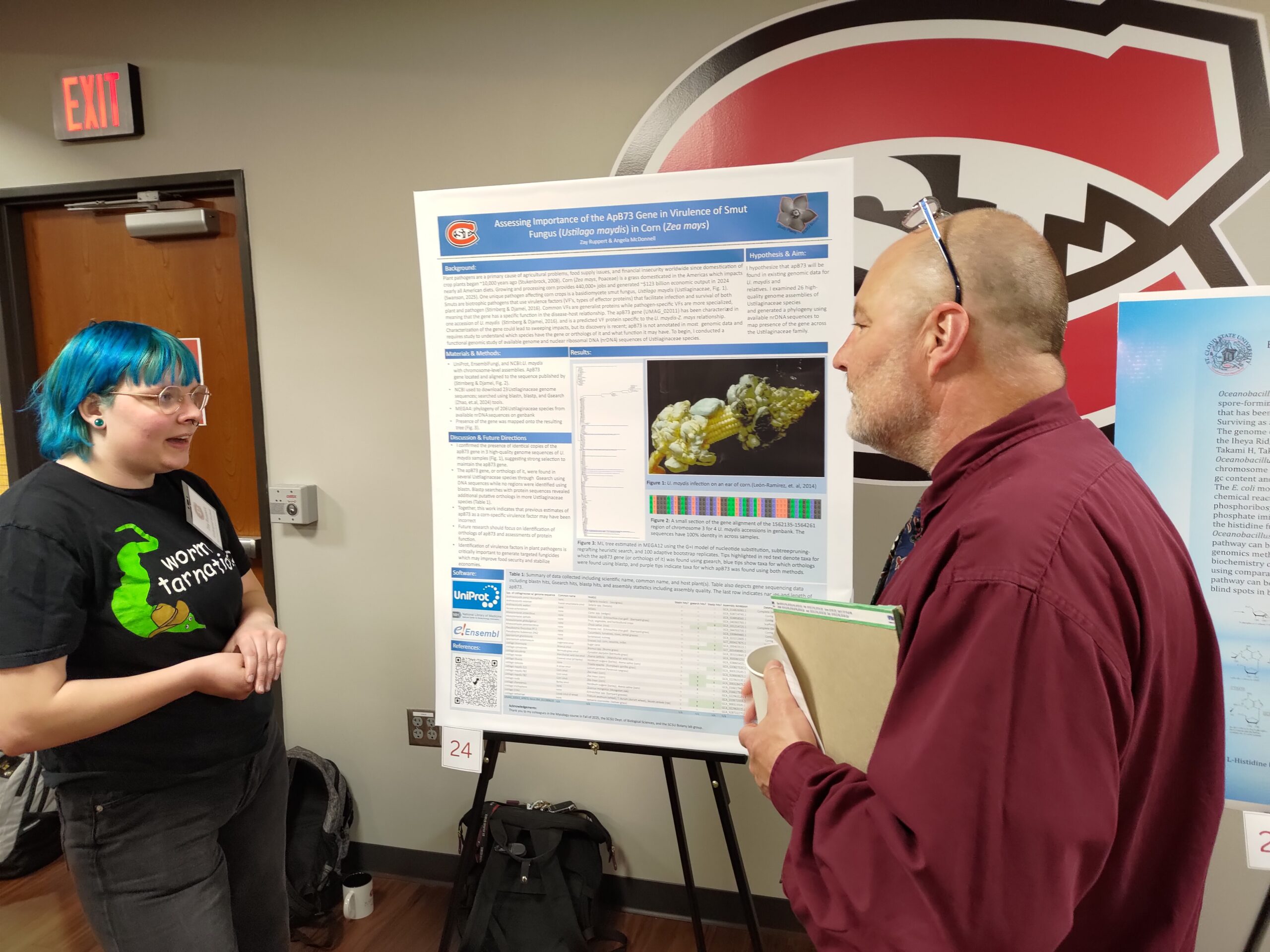 Two people talking in front of a poster board.