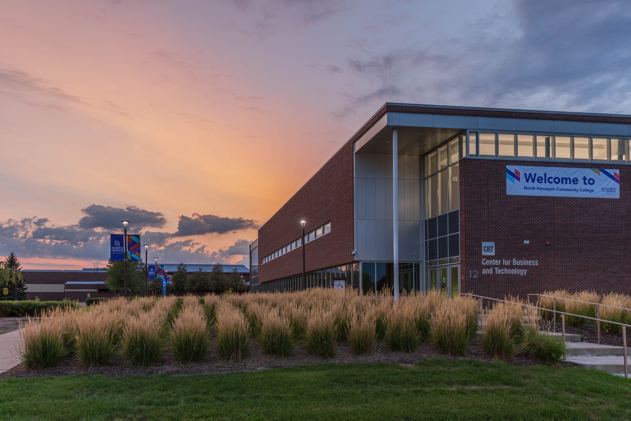 The North Hennepin Community College Center for Business and Technology building is pictured at sunset next to grass and a set of stairs