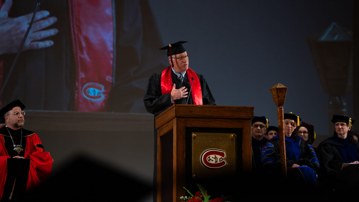 David Silker, dressed in a black graduation gown, speaks to an audience during Commencement