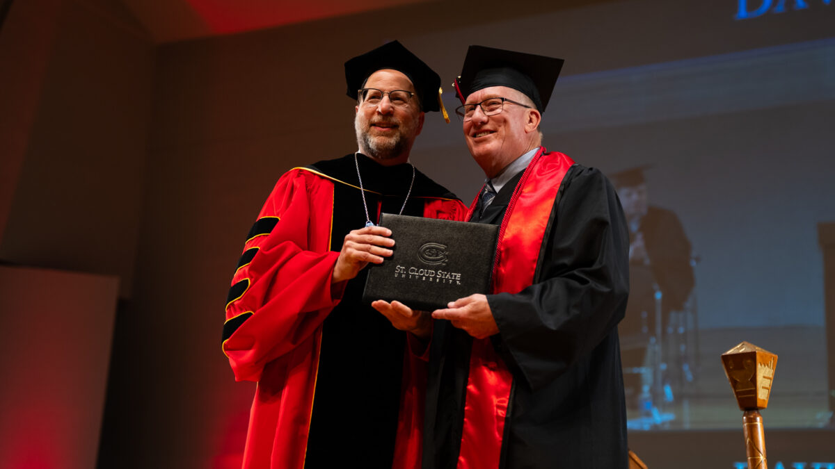 David Silker, dressed in a black graduation gown, smiles next to SCSU President Gregory Tomso