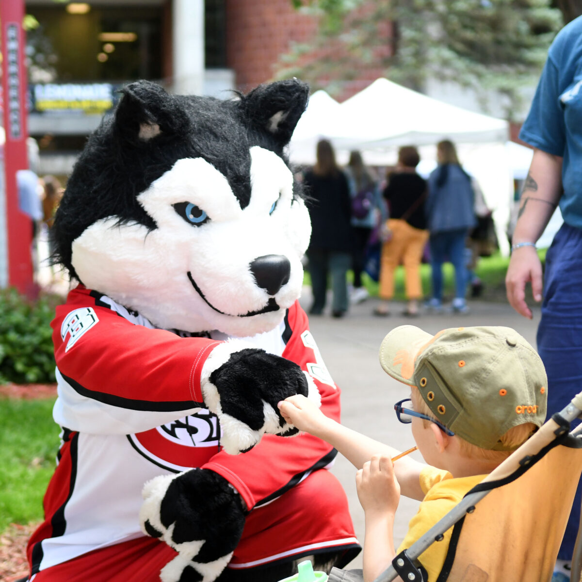 SCSU's mascot Blizzard, wearing a red and white jersey, fist bumps a child wearing glasses and a hat