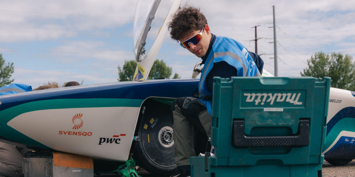 A man in sunglasses looks back at a toolbox while working on a solar-powered car