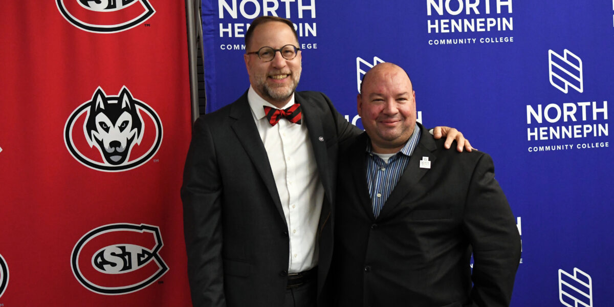Two men in suits smile for a photo in front of logos for St. Cloud State and North Hennepin Community College