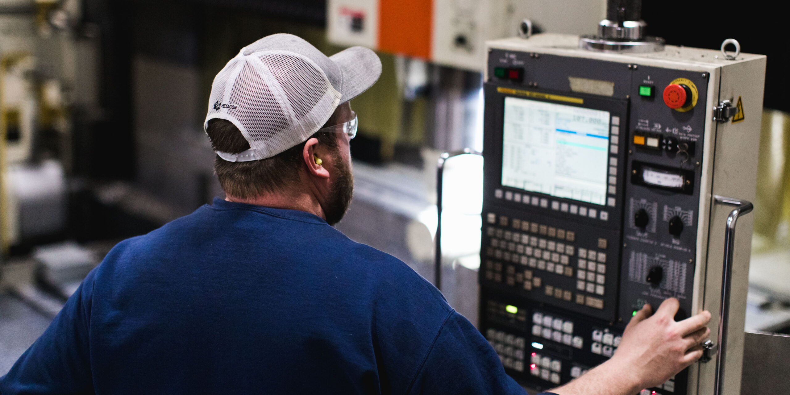 A man in a blue shirt and baseball cap turns a dial on a machine