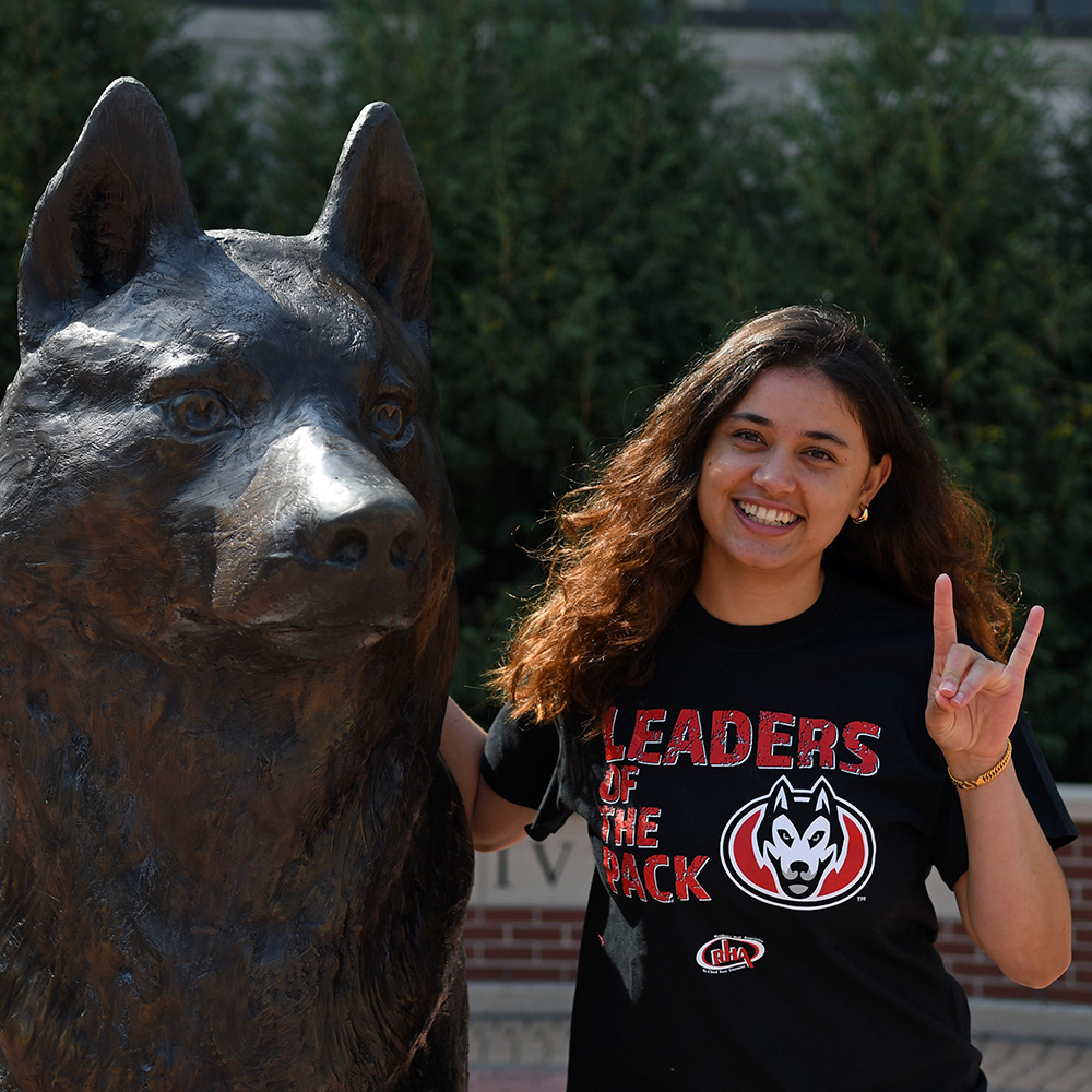 A woman in a black t shirt smiles next to a Husky statue