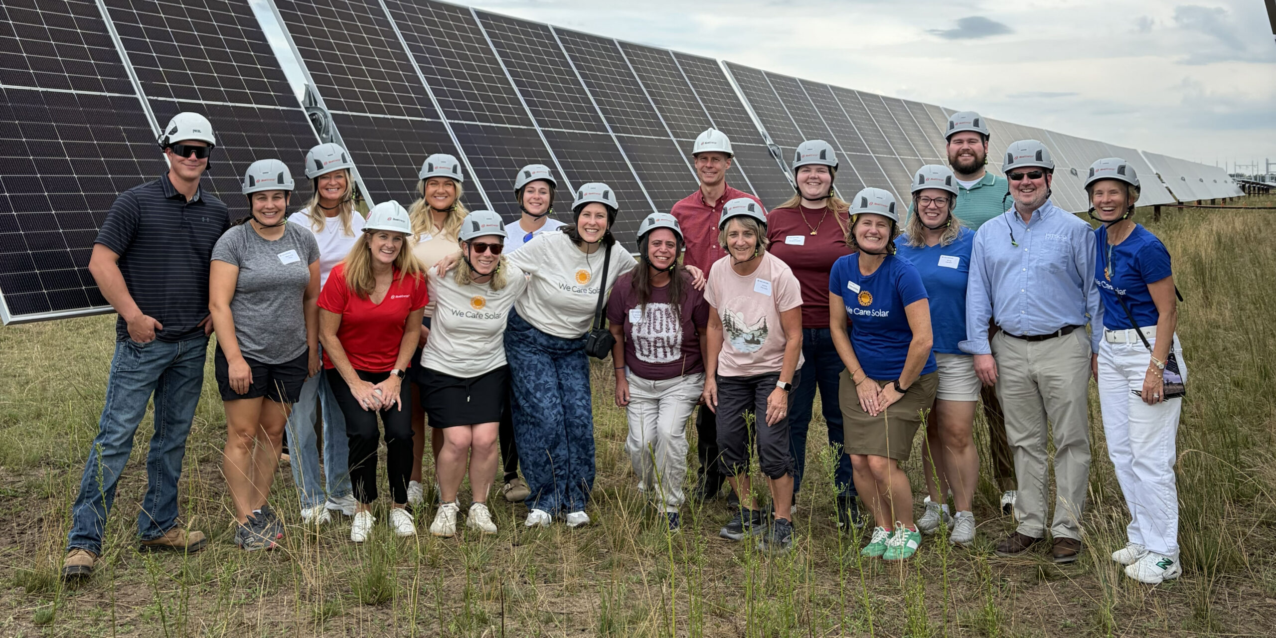 A group of 17 people in hard hats stand in front of solar panels