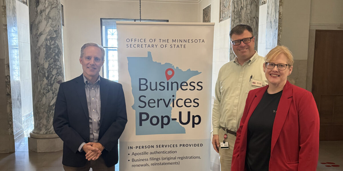 Two men and a woman smile next to a banner for the Business Services Pop-Up event