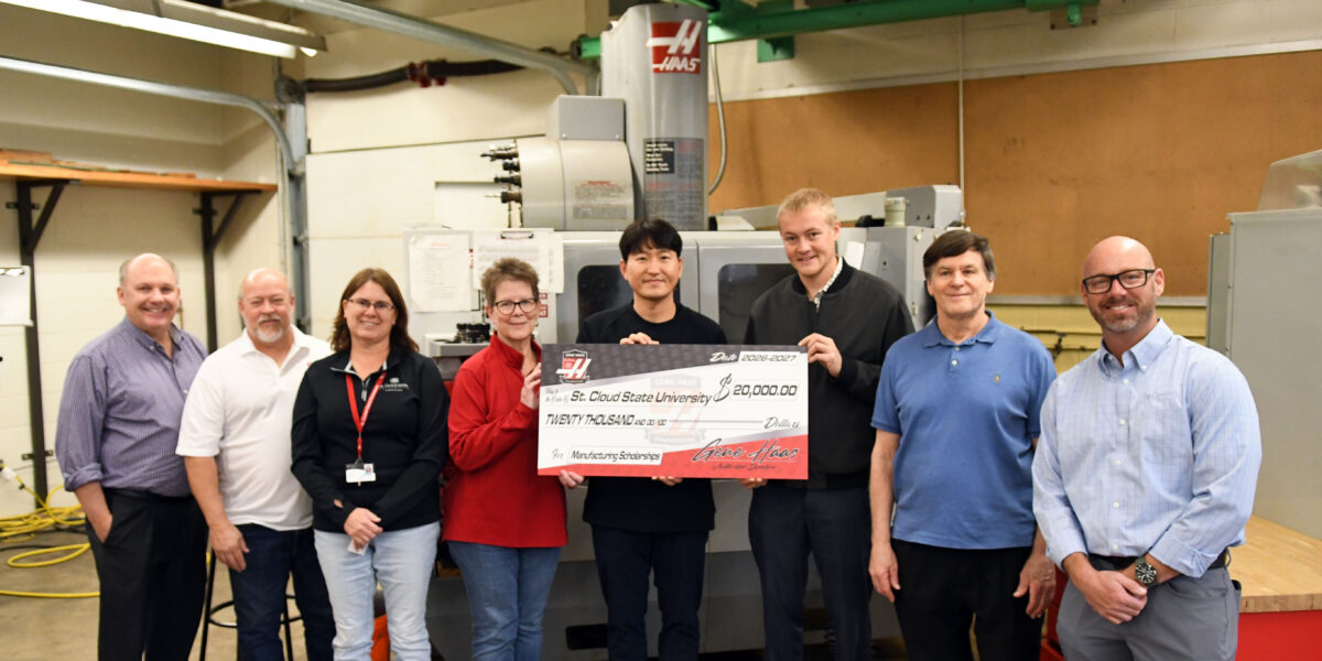 Eight people smile for a photo while holding a large check for $20,000