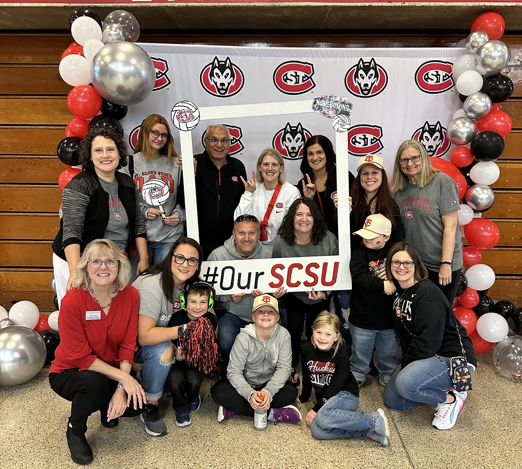 A group of people in SCSU gear smile for a photo in Halenbeck Hall