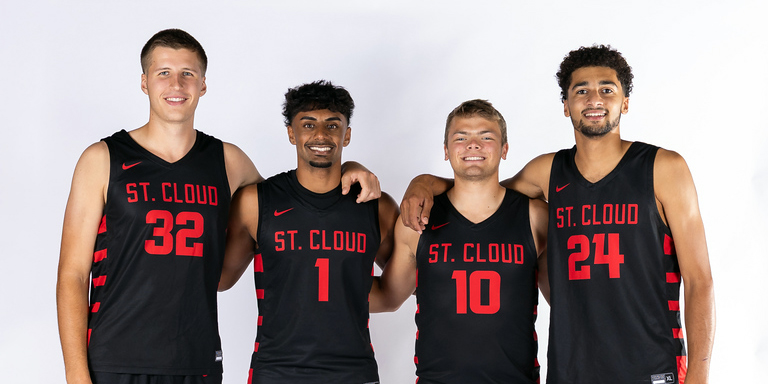 4 SCSU basketball players in black jerseys smile for a photo