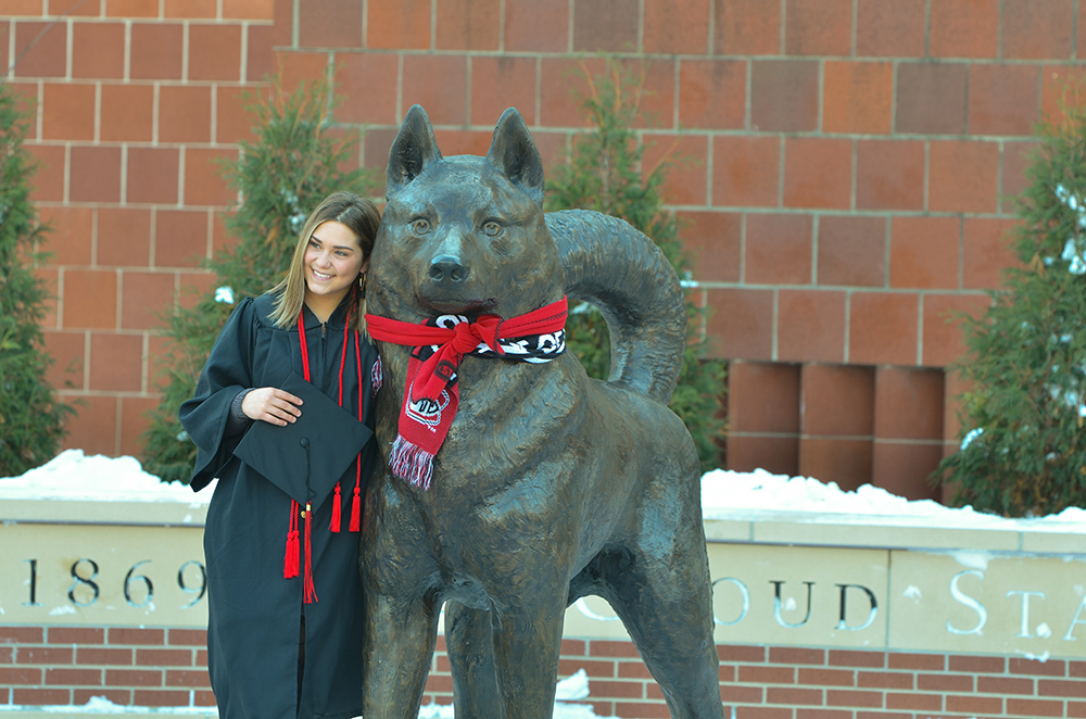 A graduate poses with the Husky statue
